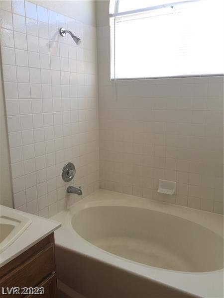 Tiled walls surround a deep soaking tub positioned beneath a large window.