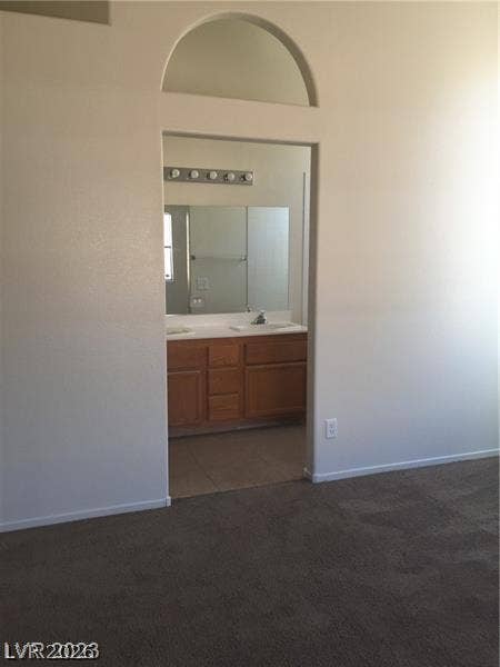 An arched doorway leads from the carpeted bedroom into an attached bathroom vanity area.