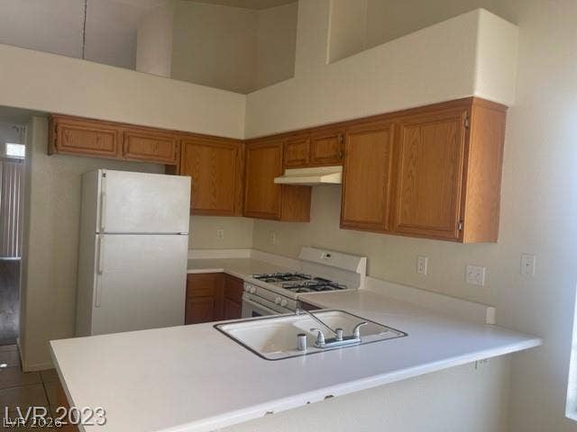 Vaulted ceilings soar over a practical kitchen featuring wood cabinetry and an integrated breakfast bar.