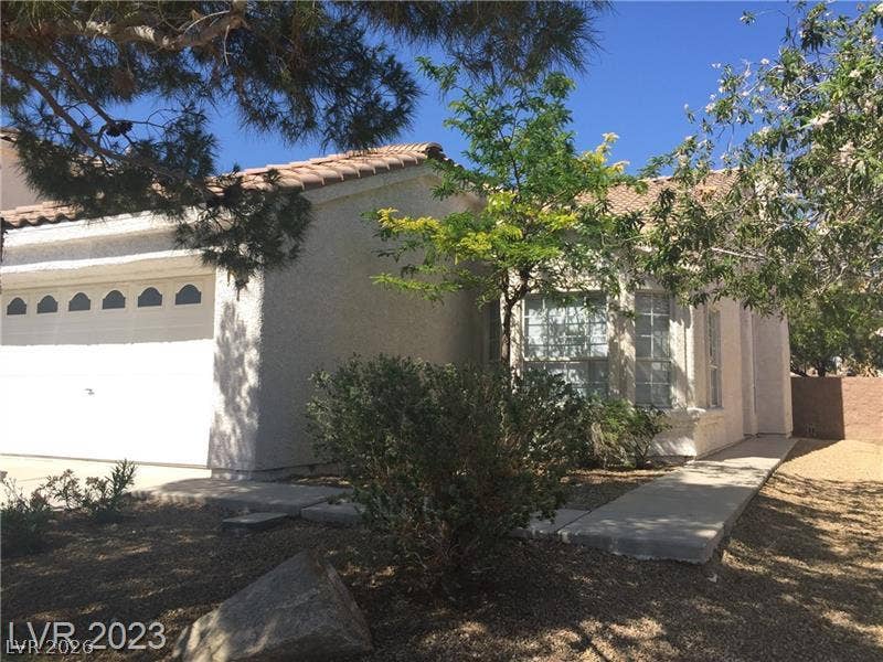 A classic stucco exterior features a tile roof and a concrete pathway leading home.