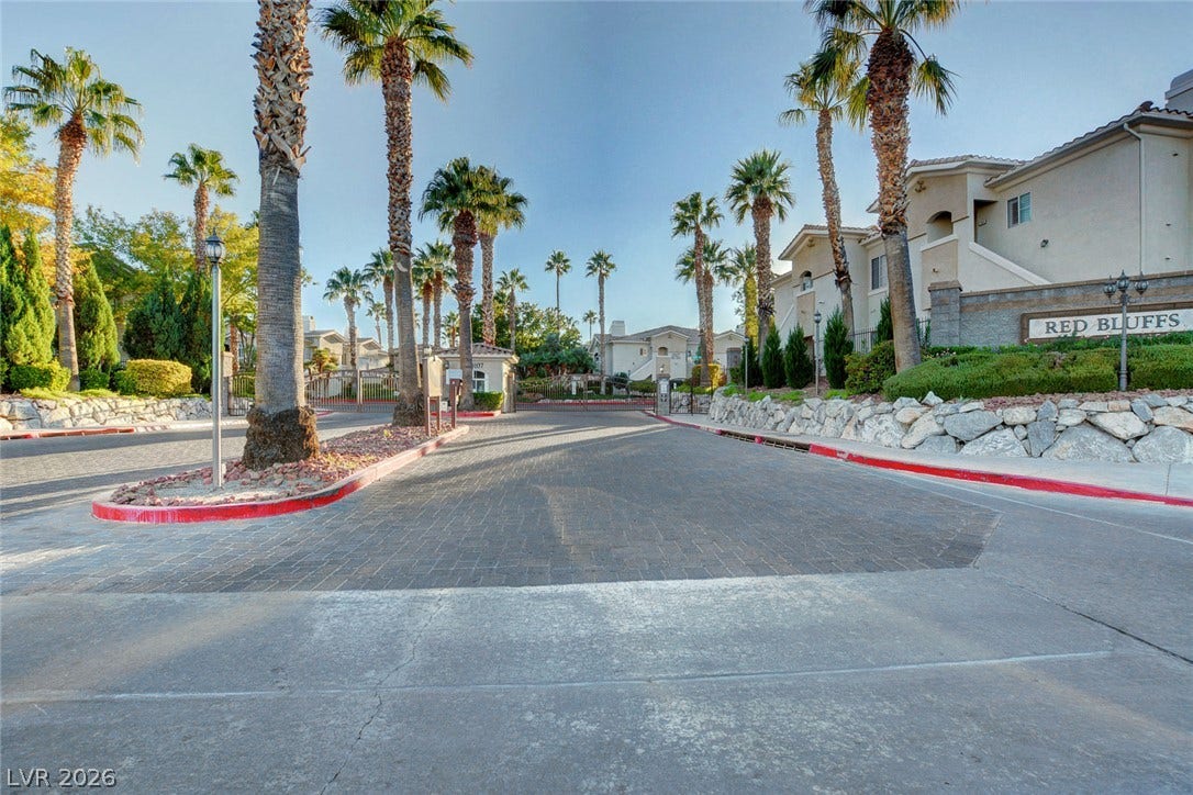 1520 Ruby Cliffs Lane, #203, Las Vegas, NV 89144 Mature palms line a paved gated entrance flanked by stone retaining walls and stucco buildings.