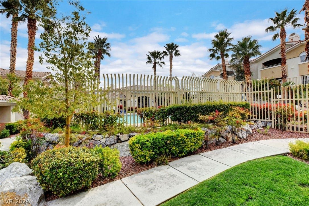 1520 Ruby Cliffs Lane, #203, Las Vegas, NV 89144 Manicured pathways and lush plantings wind past secure metal fencing under a bright sky.