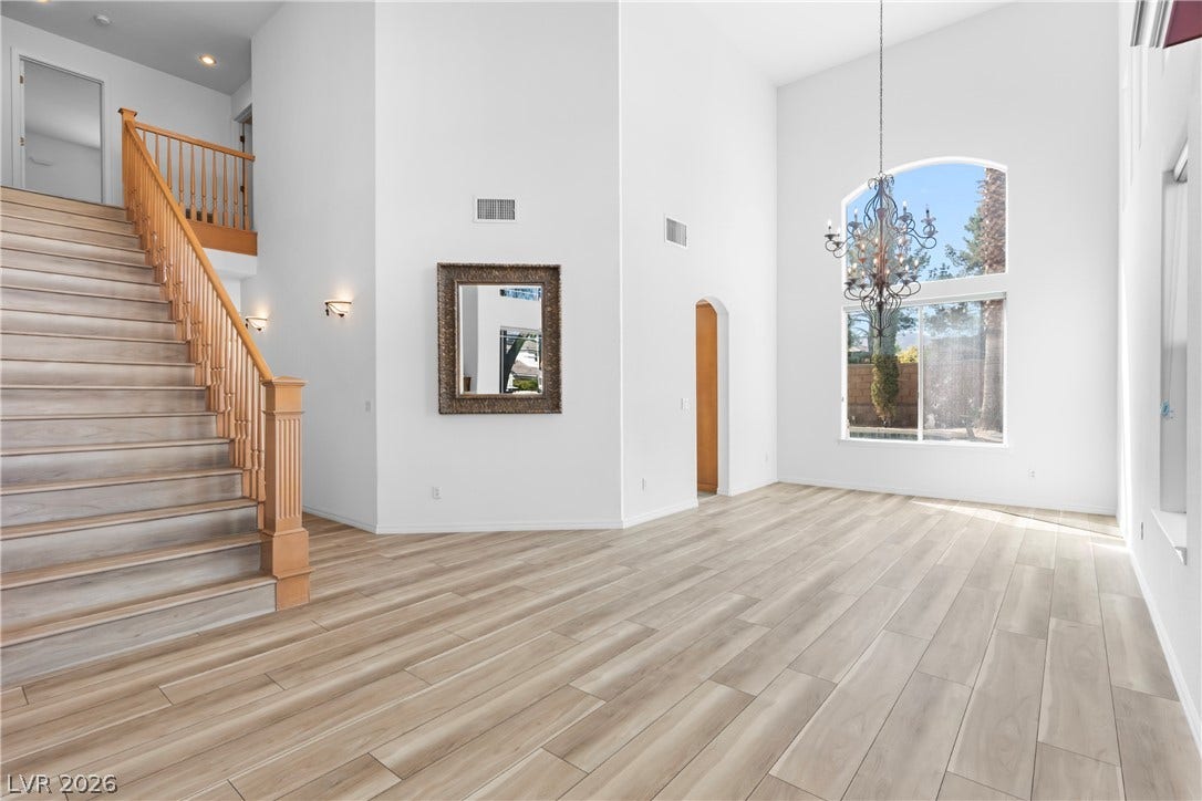 Two-story volume ceiling great room featuring light-toned wood flooring and a grand arch window.