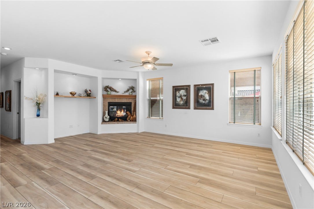 Warm, inviting living area features a corner fireplace, built-in shelving, and light wood flooring.
