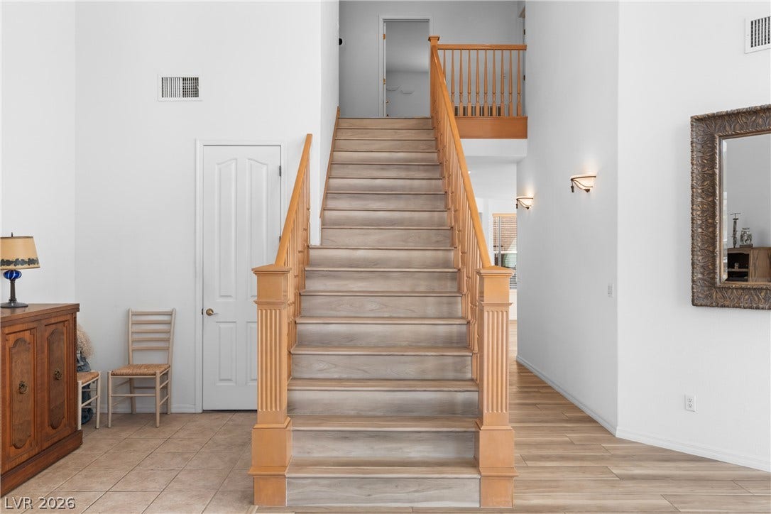 A grand central staircase with rich wood banisters welcomes visitors, complemented by modern wall sconces.