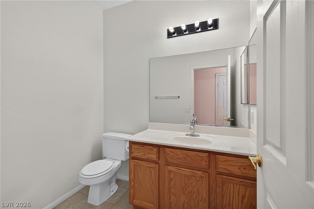 4871 Lionesse Court, Las Vegas, NV 89130 An elegant vanity with oak cabinetry and a broad mirror serves this neat half bath.