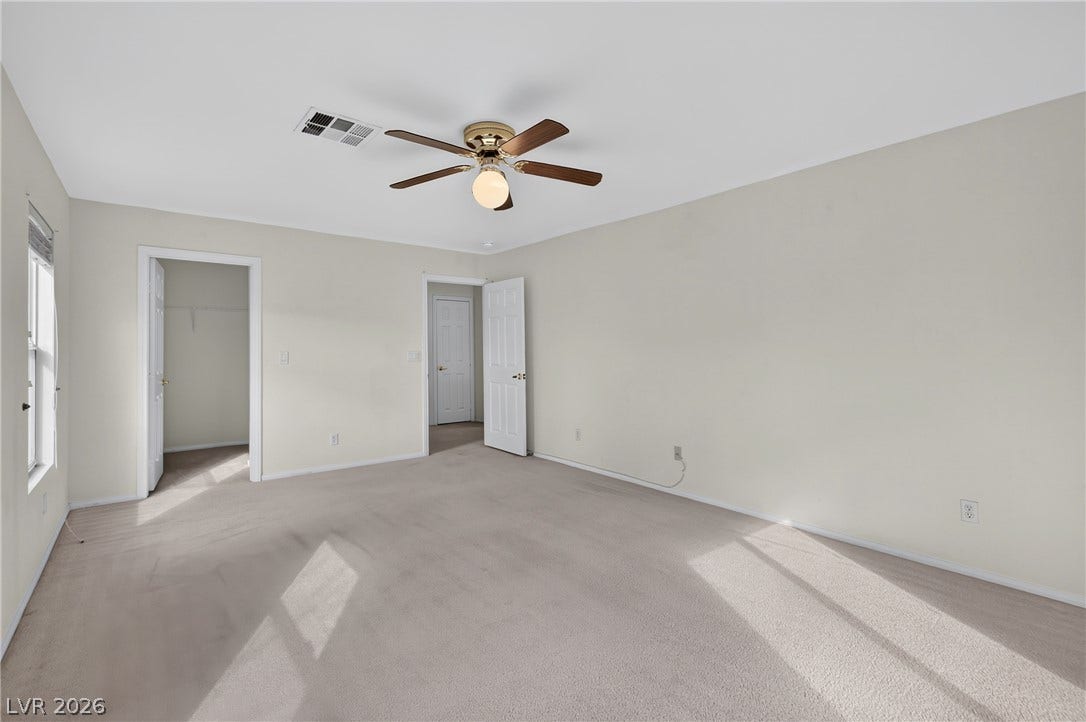 4871 Lionesse Court, Las Vegas, NV 89130 Natural light streams across a spacious bedroom featuring soft neutral walls and comfortable carpeting.