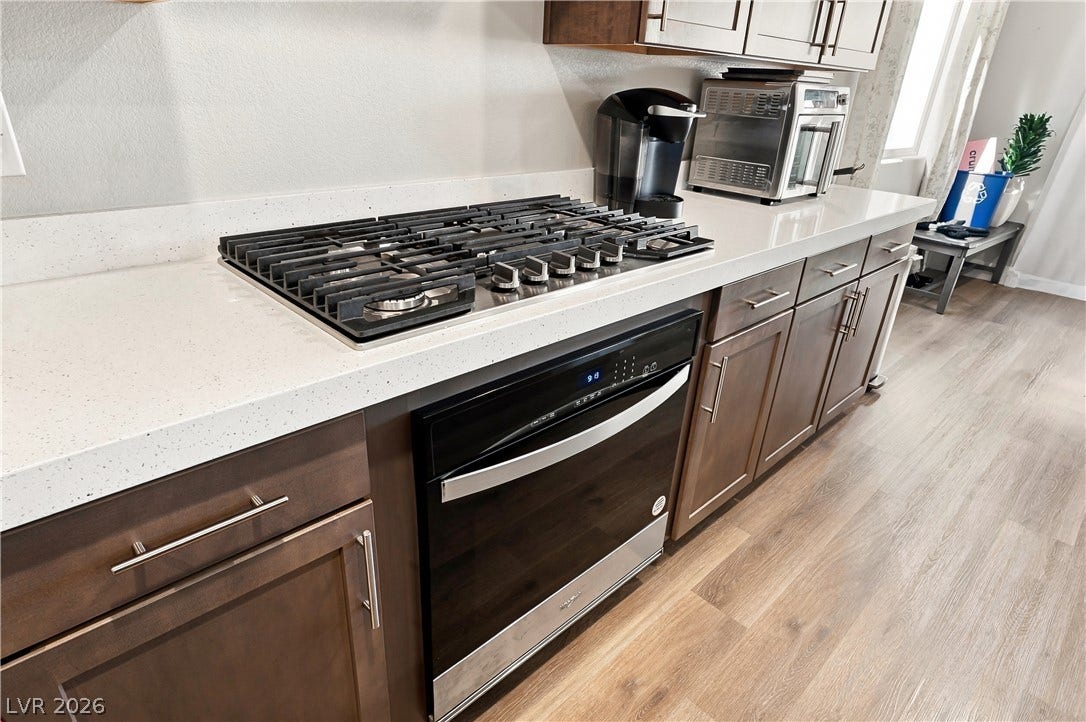 Gleaming stone countertops flank a modern gas cooktop above durable wood-plank flooring.