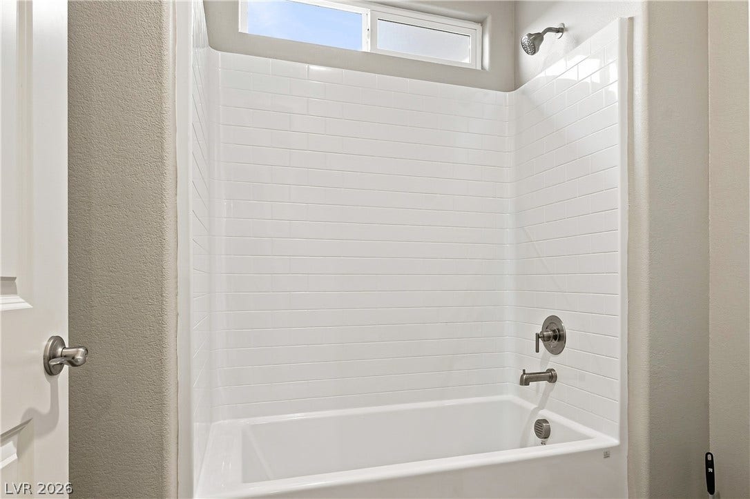 Tiled shower walls surround a built-in bathtub illuminated by natural light from a transom window.
