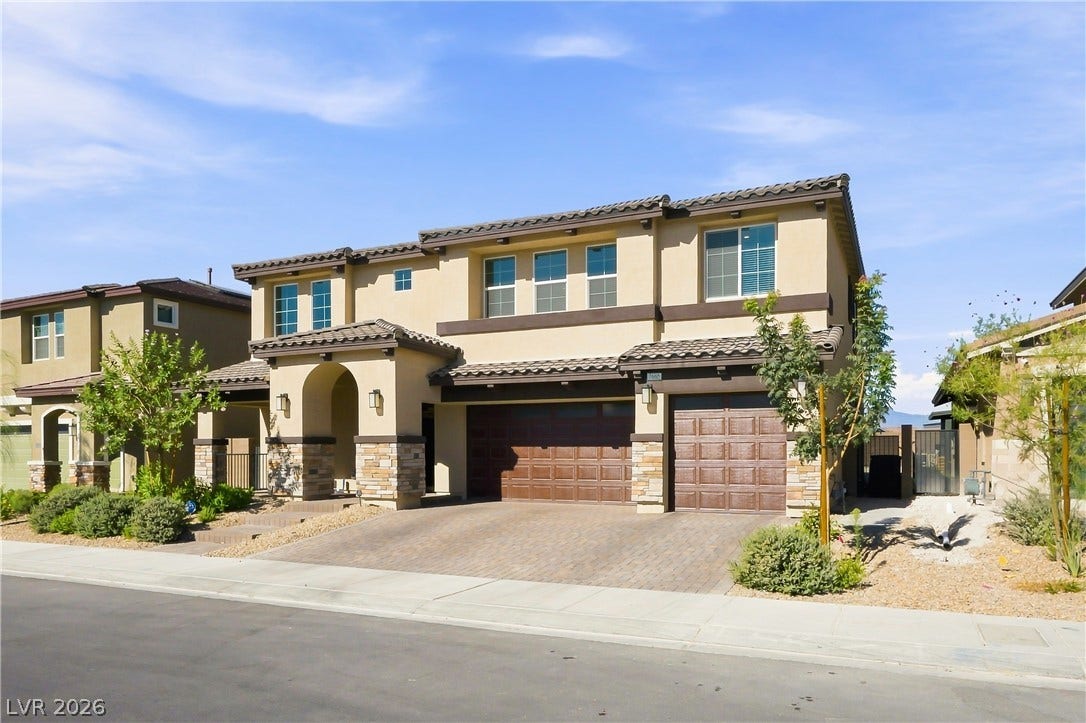An arched covered entry and paved driveway welcome visitors to this modern two-story home.