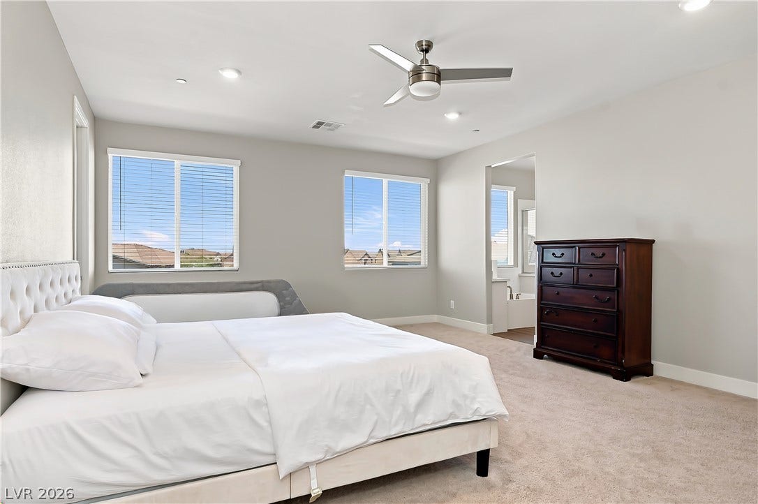 Plentiful natural light fills a spacious bedroom complete with neutral carpeting and an ensuite bath.