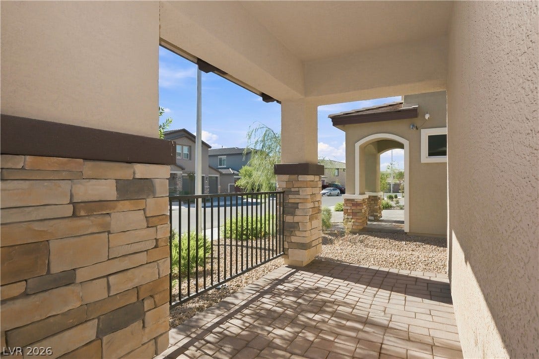 An inviting covered entry features stone pillars and a paved walkway leading to the courtyard.