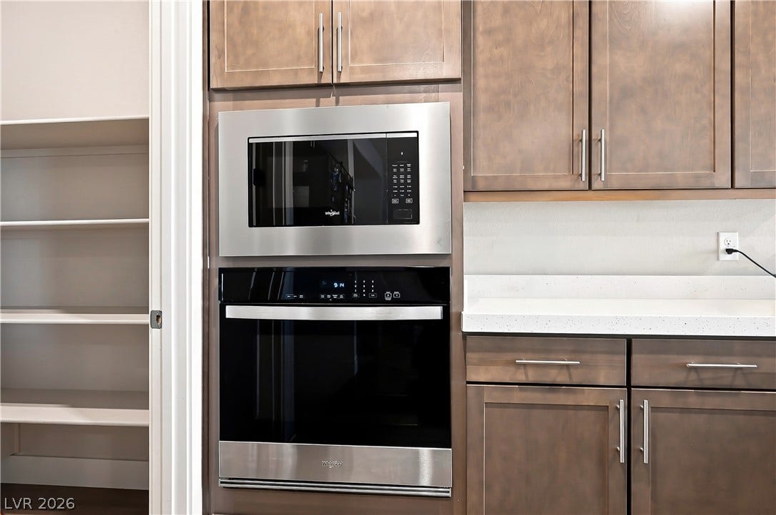 Rich wood cabinetry surrounds modern built-in appliances adjacent to a spacious walk-in pantry.