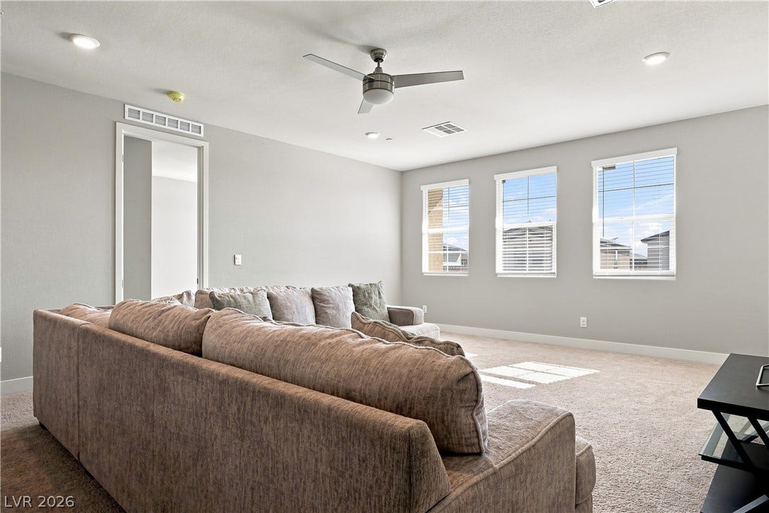 A spacious secondary living space features plush carpet, recessed lighting, and large windows.