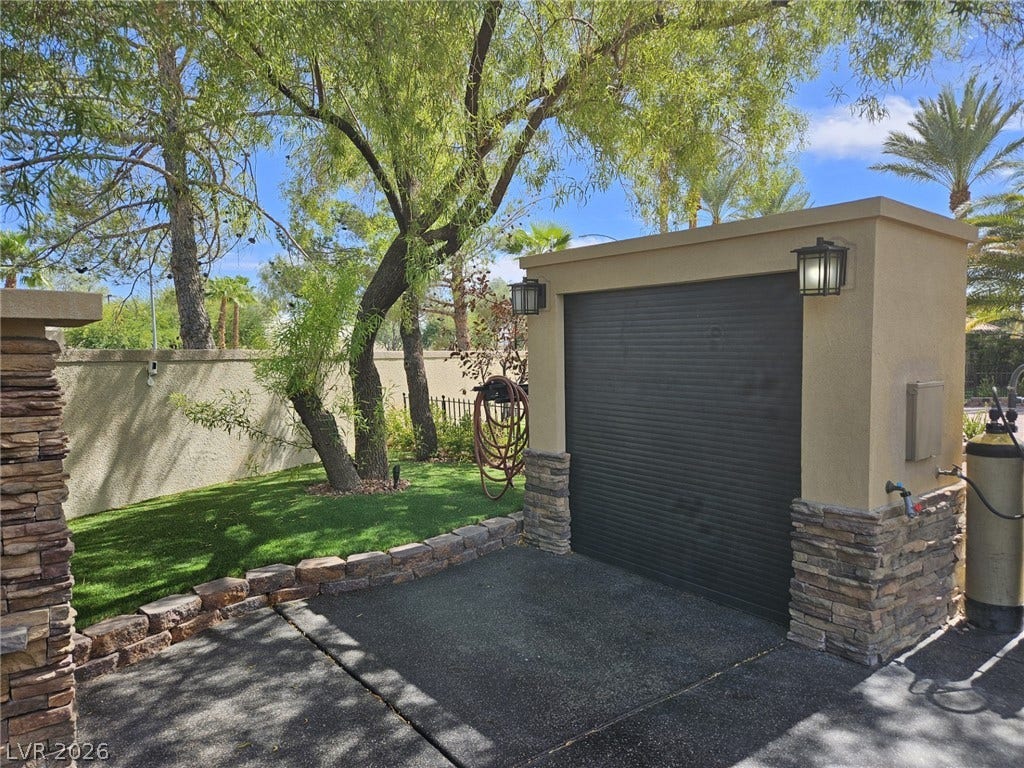 8175 Arville Street, #32, Las Vegas, NV 89139 A detached stone-accented garage structure sits adjacent to a landscaped lawn with mature trees.