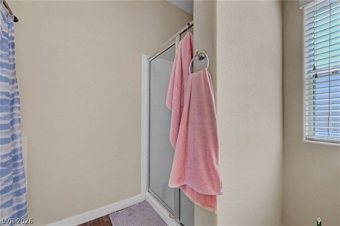 7450 S Eastern Avenue, #1064, Las Vegas, NV 89123 A glass-enclosed shower is flanked by neutral walls and a window with blinds.