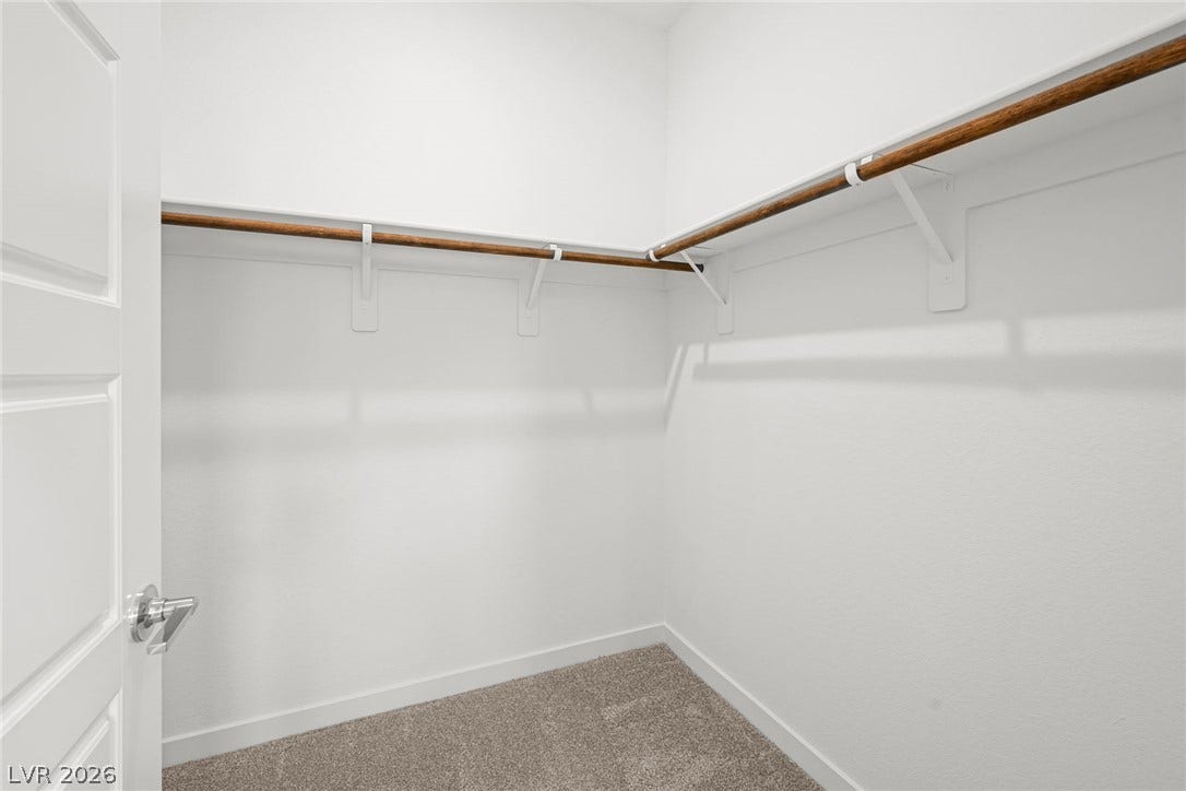 9568 Sagebrush Grove Street, Las Vegas, NV 89178 A spacious walk-in closet features plush carpeting alongside wooden hanging rods and built-in shelving.