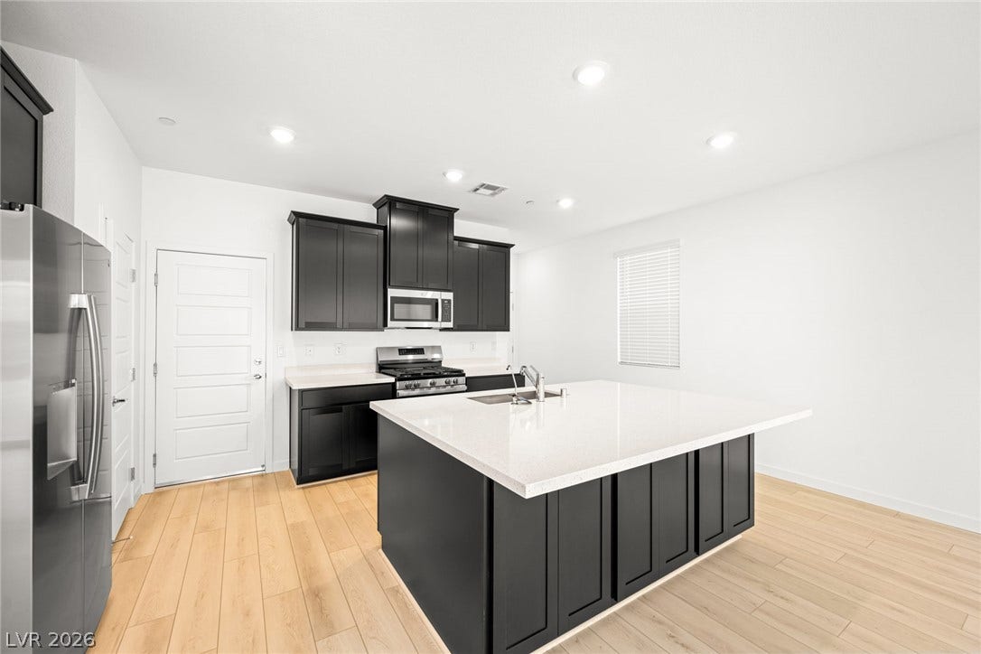 9568 Sagebrush Grove Street, Las Vegas, NV 89178 Crisp white walls and warm wood flooring frame a contemporary kitchen with dark cabinetry.