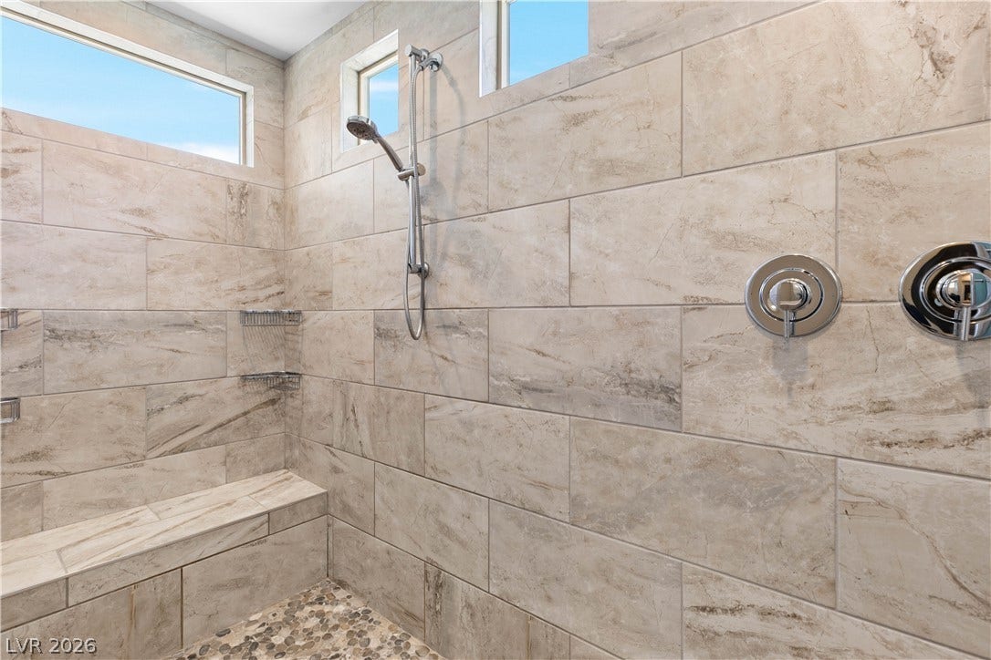 2999 The Peaks Lane, Las Vegas, NV 89138 Floor-to-ceiling tilework and high transom windows elevate this walk-in shower. Upstairs Primary bedroom (5)with large sitting area/gym separated by beautiful double sided fireplace. Huge Custom walk-in closet and highly upgraded primary bathroom and private balcony.
