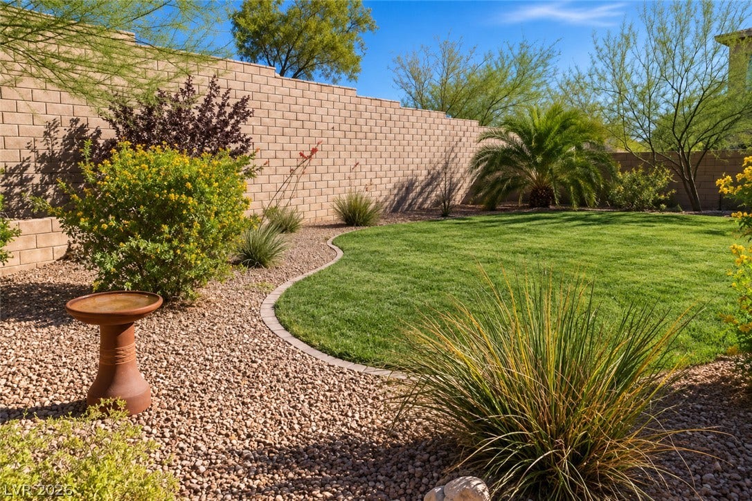 11886 Corenzio Avenue, Las Vegas, NV 89138 A curved green lawn is bordered by gravel landscaping and a tall block privacy wall.