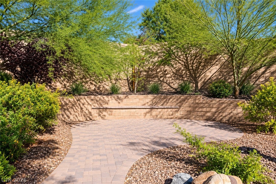 11886 Corenzio Avenue, Las Vegas, NV 89138 A curved paver patio is bordered by stone retaining walls and mature desert landscaping.