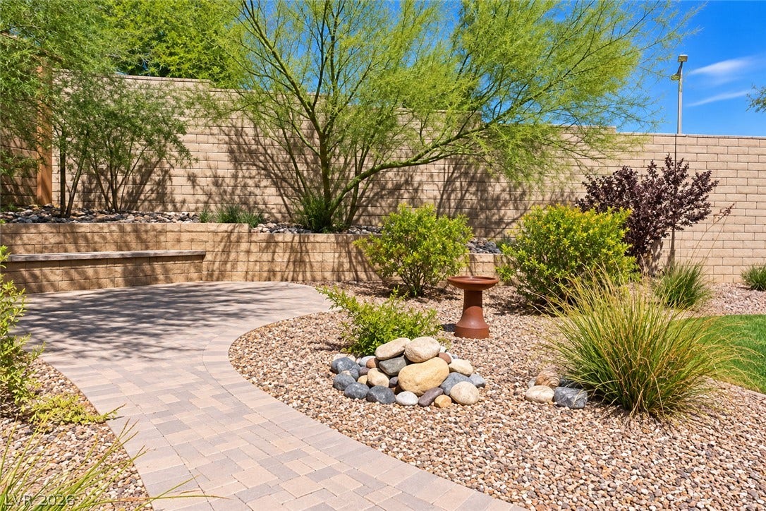 11886 Corenzio Avenue, Las Vegas, NV 89138 A curved paver patio leads through meticulously landscaped grounds bordered by high stone retaining walls.