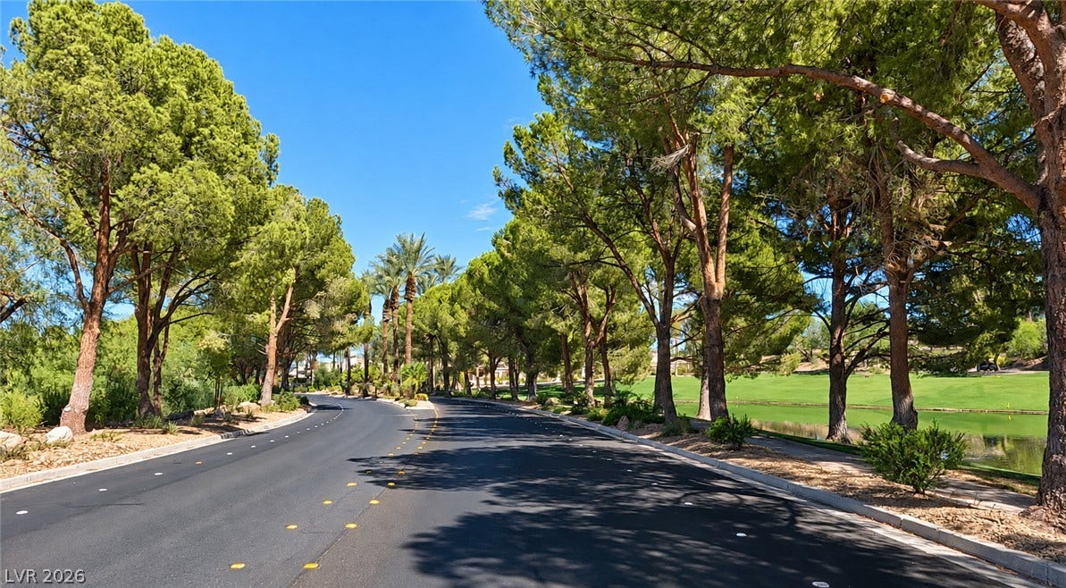10 Caminito Amore, Henderson, NV 89011 Mature trees line a winding paved roadway bordering a scenic neighborhood golf course and pond.