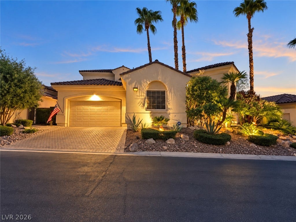 10 Caminito Amore, Henderson, NV 89011 Lush desert landscaping accents this Mediterranean-style exterior with a paved driveway under a twilight sky.