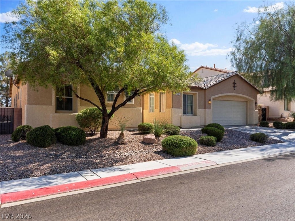 1217 Silent Sunset Avenue, North Las Vegas, NV 89084 Desert landscaping and mature shade trees frame this classic stucco home with a tile roof.
