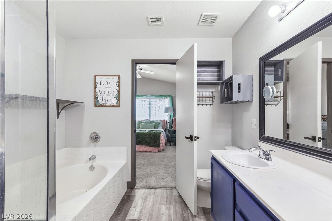 7066 Shimmering Avenue, Henderson, NV 89011 An inviting bathroom features a deep soaking tub and a vanity alongside vinyl plank flooring.