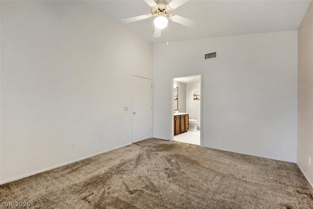 A spacious bedroom with neutral carpeting leads directly into an attached private bathroom.