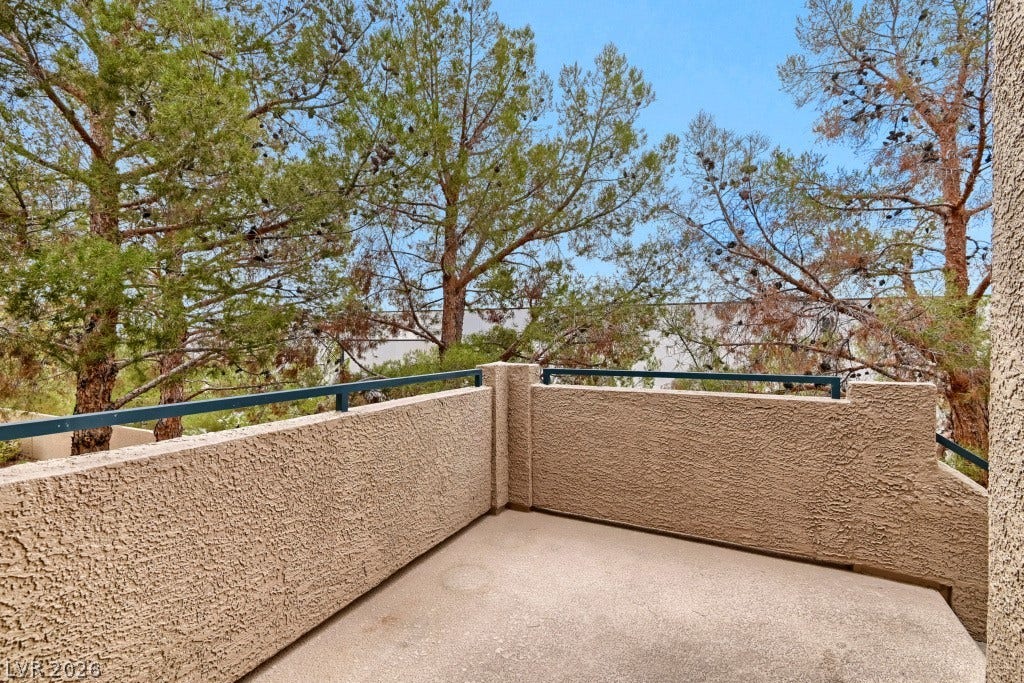 Mature green trees frame the view from this private concrete balcony with textured stucco walls.