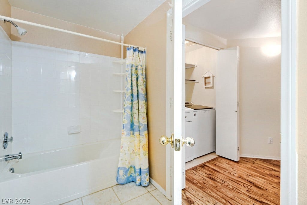A classic tiled shower tub combo sits adjacent to a convenient laundry closet area.