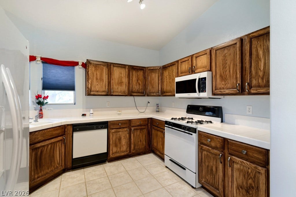 Rich wood cabinetry surrounds this kitchen equipped with tile countertops and built-in appliances.