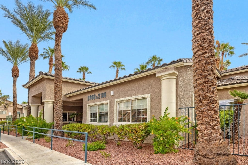 Mature palms frame this stucco exterior featuring classic architectural columns and stone landscaping.
