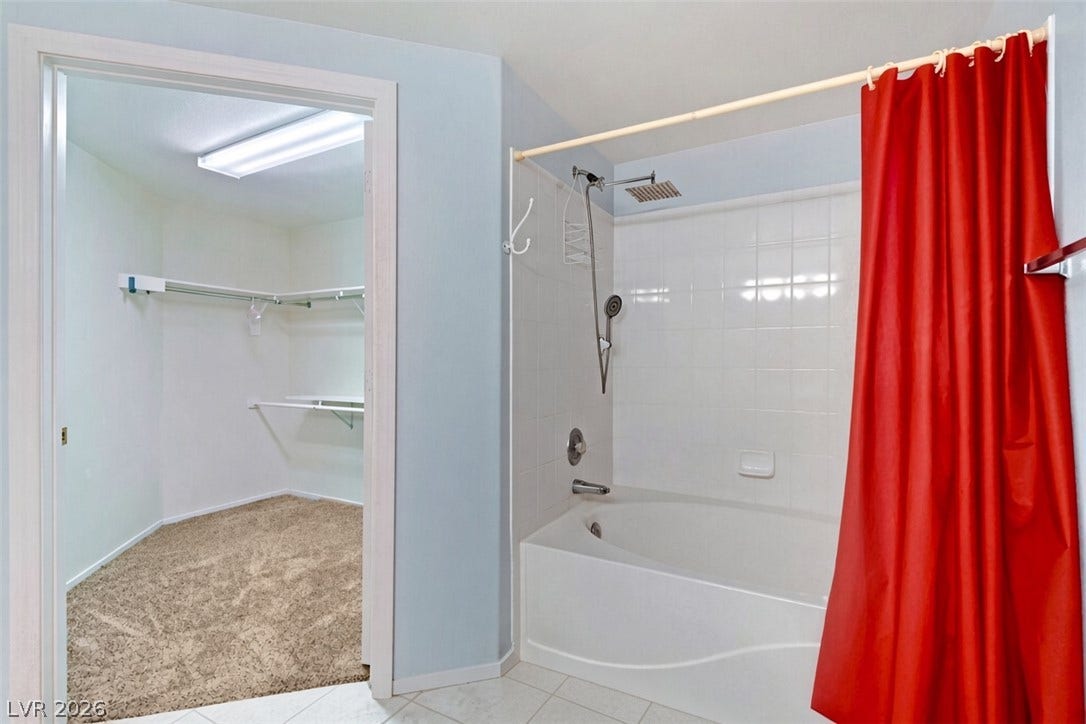 A spacious soaking tub sits adjacent to a carpeted walk-in closet.