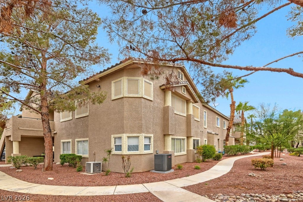 Mature desert landscaping and winding concrete pathways frame this stucco multi-family residential building.