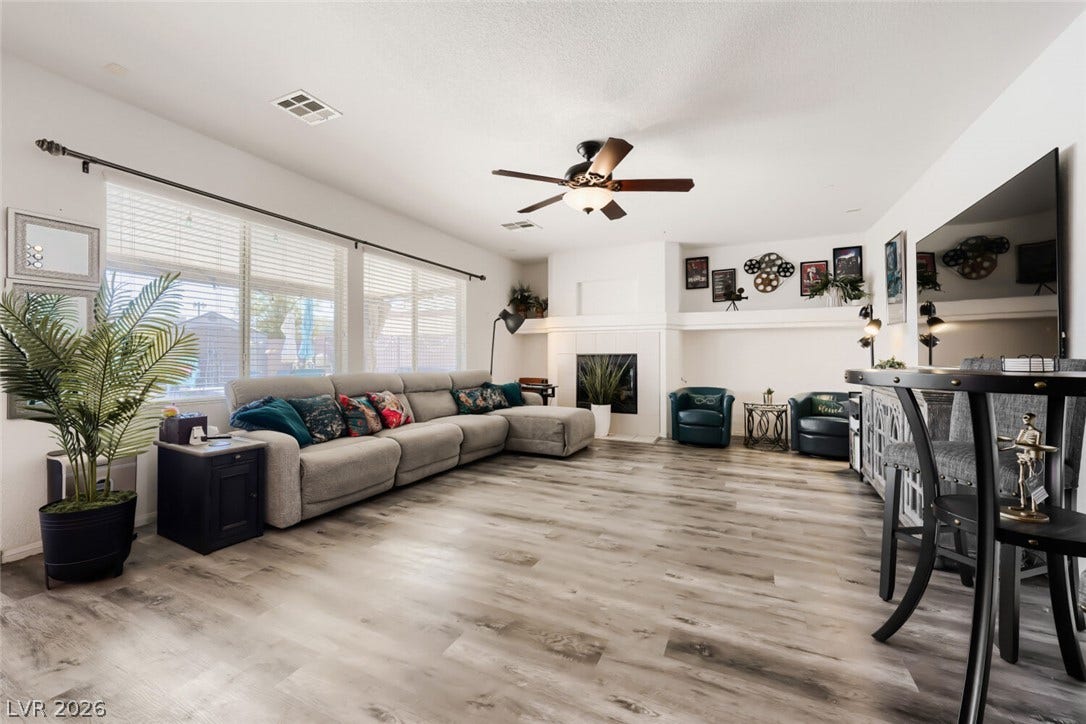 109 Spur Ranch Avenue, North Las Vegas, NV 89032 Generous windows fill this spacious living room featuring wood-style flooring and a cozy fireplace.