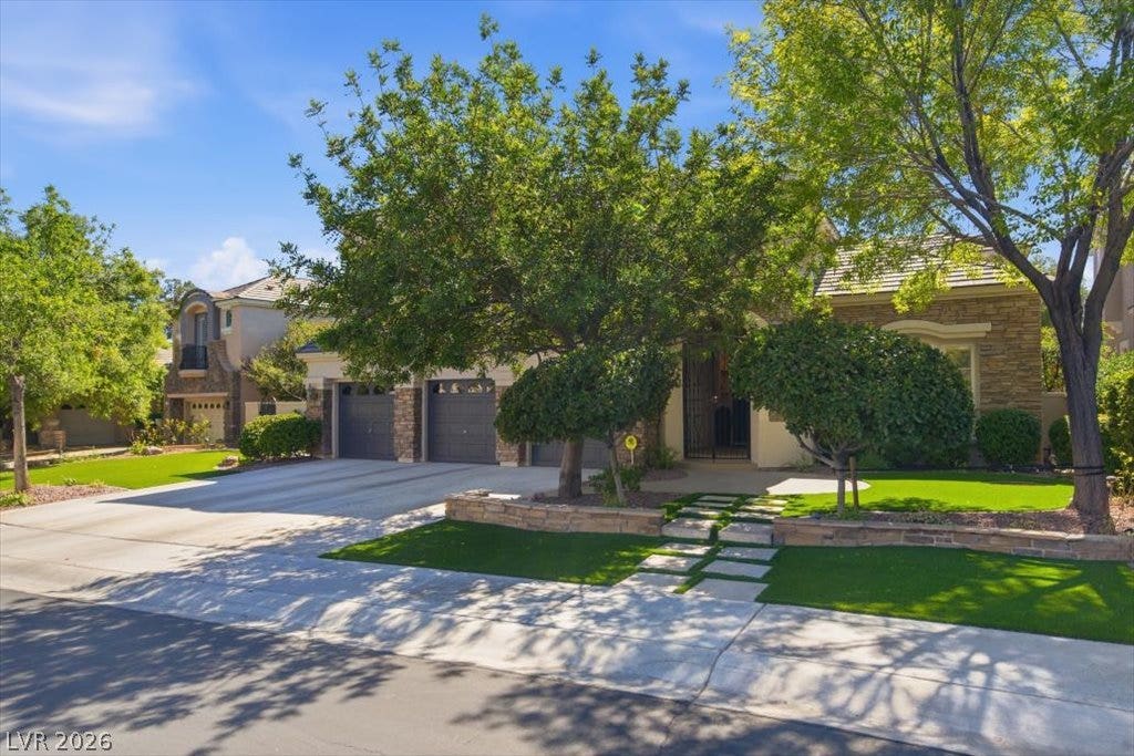 9521 Queen Charlotte Drive, Las Vegas, NV 89145 Mature trees frame a stone-accented facade featuring a spacious driveway and custom hardscaping details.