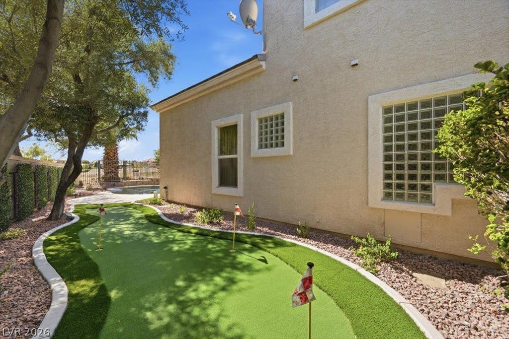 9521 Queen Charlotte Drive, Las Vegas, NV 89145 Manicured putting green lines the side of this stucco home under clear blue skies.
