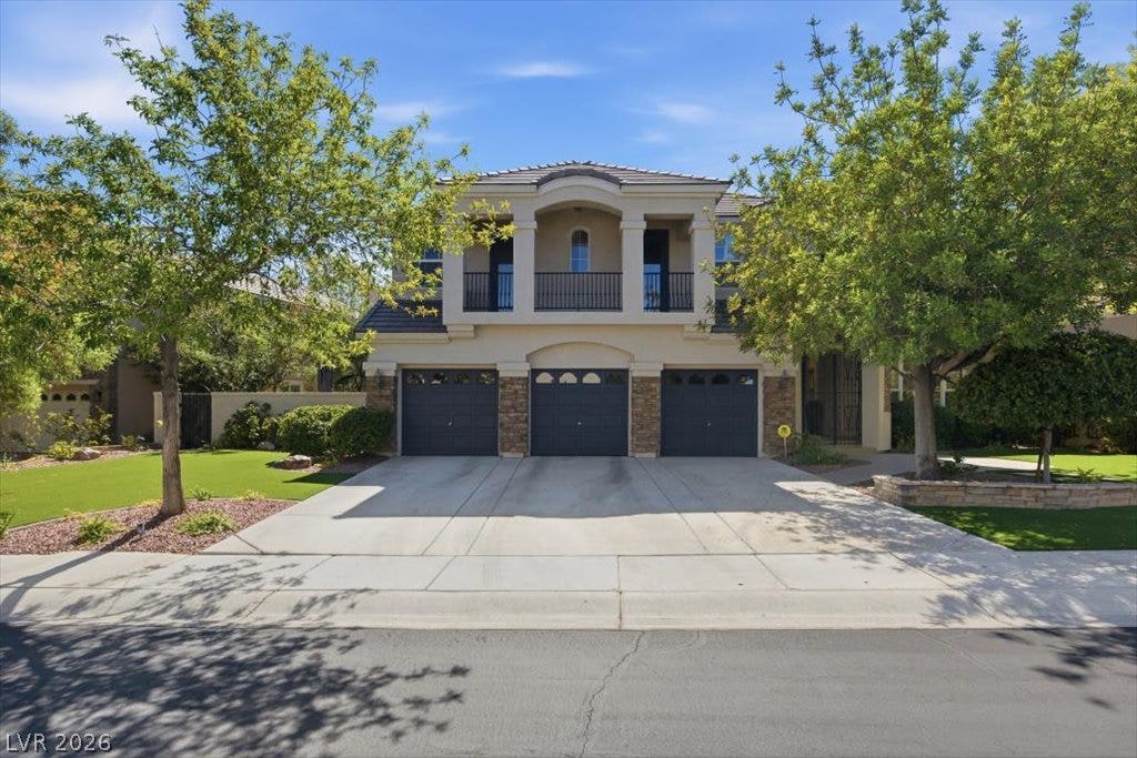 9521 Queen Charlotte Drive, Las Vegas, NV 89145 Mature trees frame a wide concrete driveway leading to the three-car garage and balcony above.