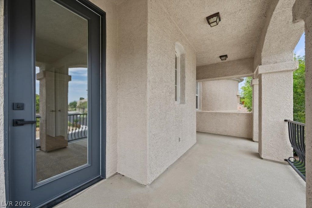 9521 Queen Charlotte Drive, Las Vegas, NV 89145 An arched covered balcony features stucco walls, concrete flooring, and a modern glass entry door.