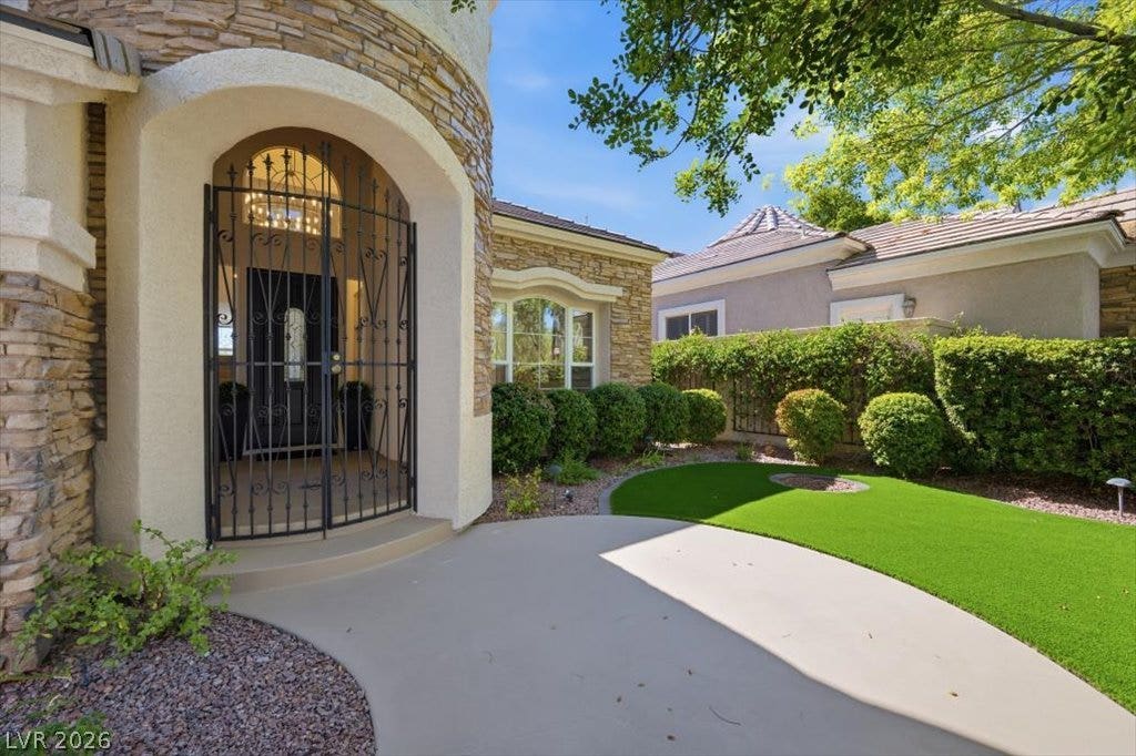 9521 Queen Charlotte Drive, Las Vegas, NV 89145 An arched entry with decorative iron gates opens to a manicured front courtyard and lawn.