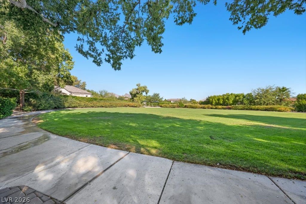 9521 Queen Charlotte Drive, Las Vegas, NV 89145 Mature trees frame a sprawling, manicured green lawn bordered by a curved concrete walkway.