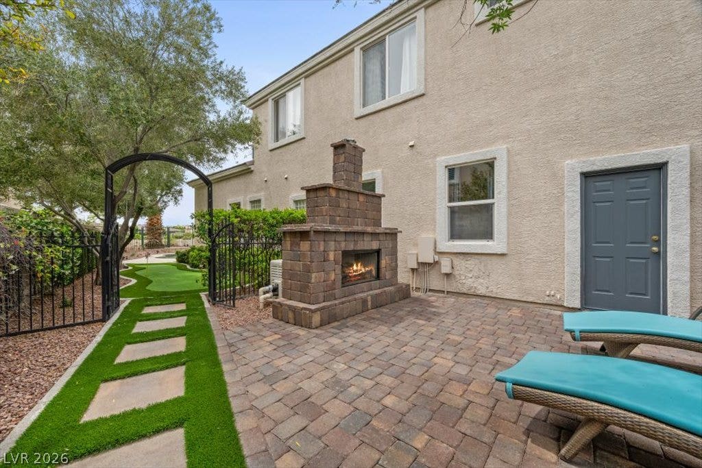 9521 Queen Charlotte Drive, Las Vegas, NV 89145 An inviting stone fireplace highlights this paved patio area alongside a neat green lawn.