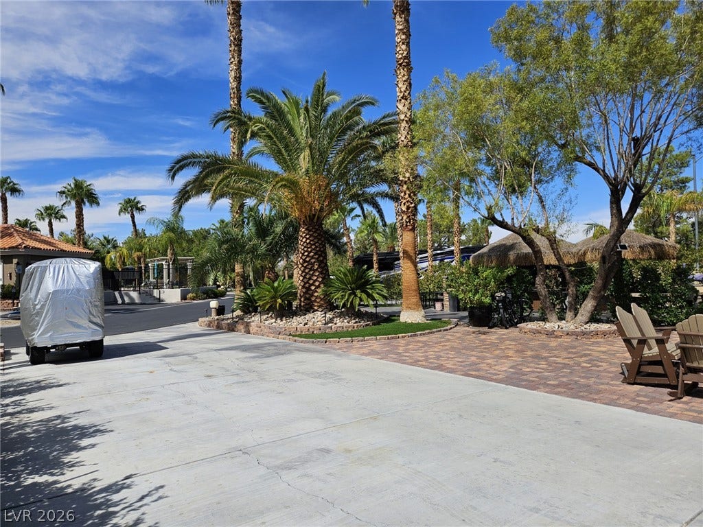 8175 Arville Street, #33, Las Vegas, NV 89139 Lush palm trees and meticulous paving create a resort-style driveway entrance under clear blue skies.