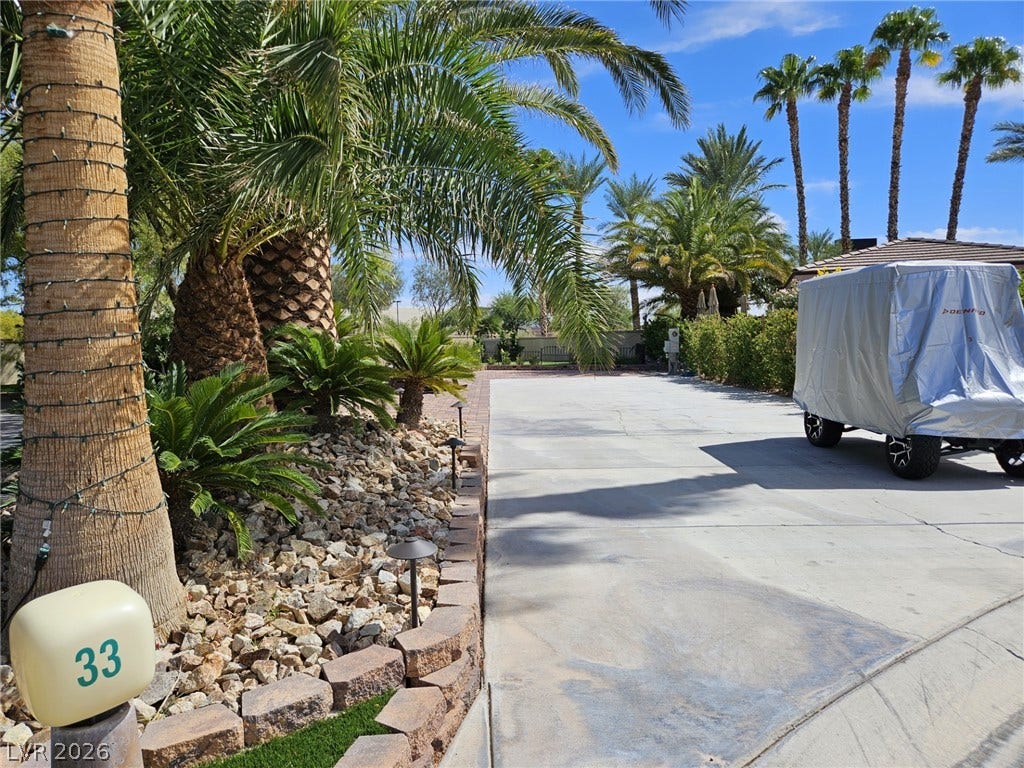 8175 Arville Street, #33, Las Vegas, NV 89139 Lush palm trees and neat stone landscaping border a spacious concrete driveway under sunny skies.