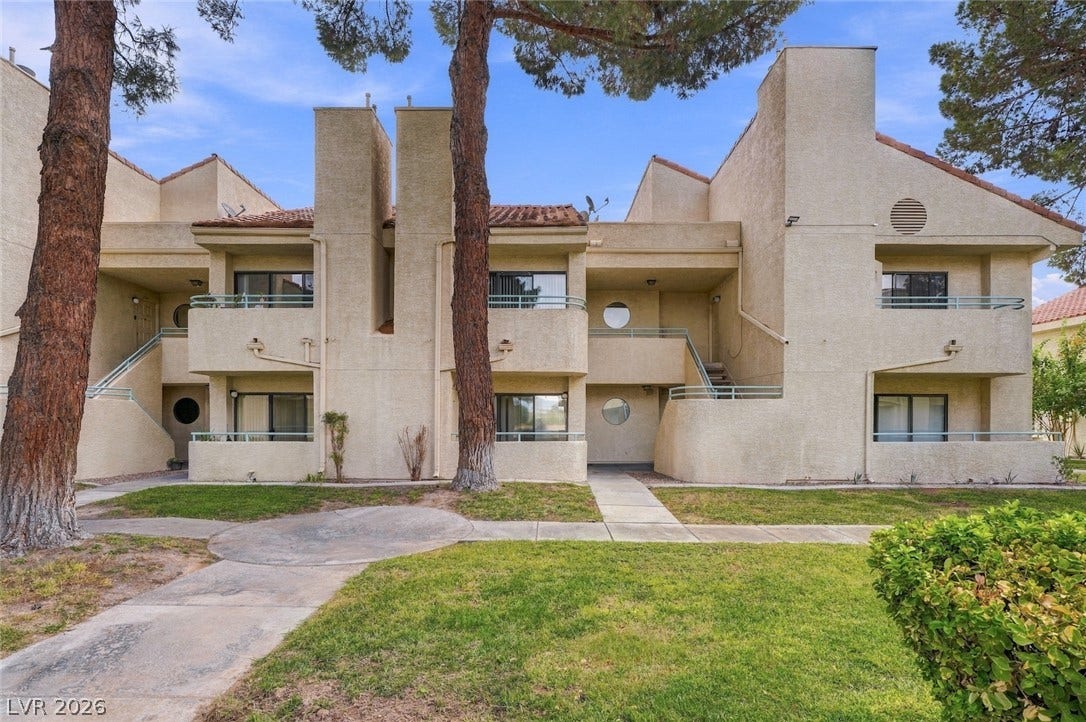 830 N Sloan Lane, #202, Las Vegas, NV 89110 Mature trees frame the stucco exterior of this multi-level residential building with private balconies.