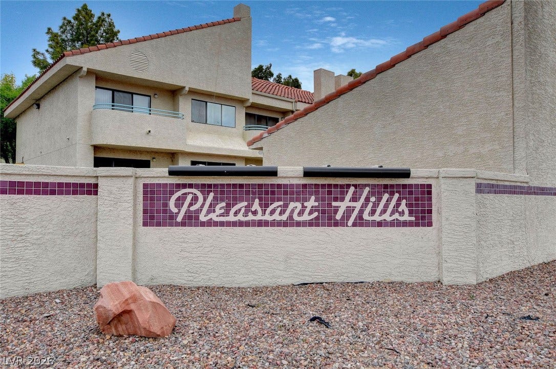 830 N Sloan Lane, #202, Las Vegas, NV 89110 A prominent neighborhood entry sign sits framed by stucco walls and tile roofing.