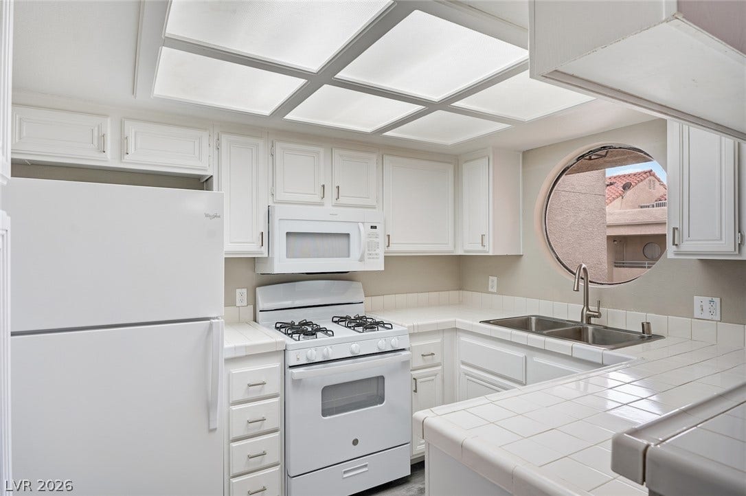 830 N Sloan Lane, #202, Las Vegas, NV 89110 A circular window anchors this well-equipped kitchen featuring tiled countertops and classic cabinetry.